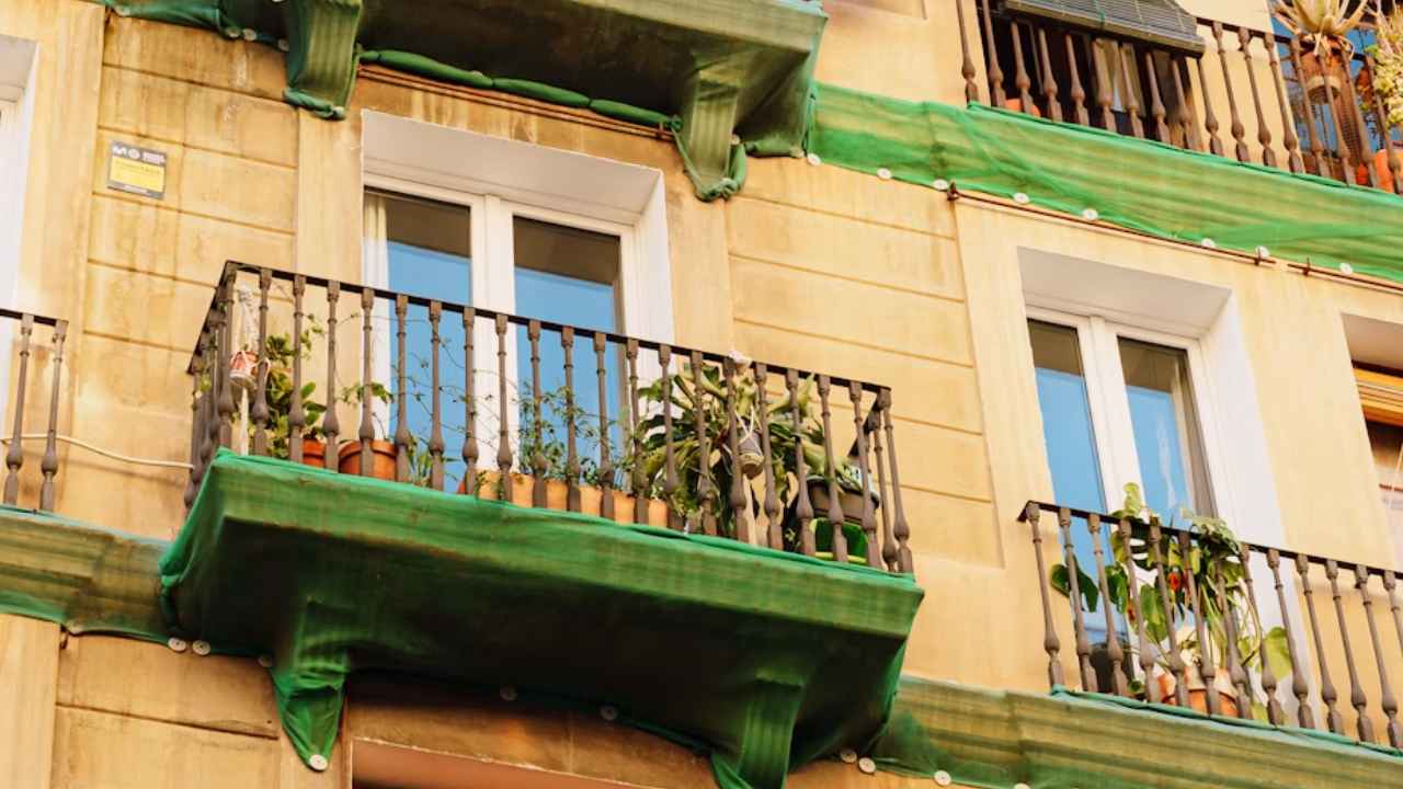 Fachada de un edificio de Barcelona con balcones verdes, plantas y toldos.