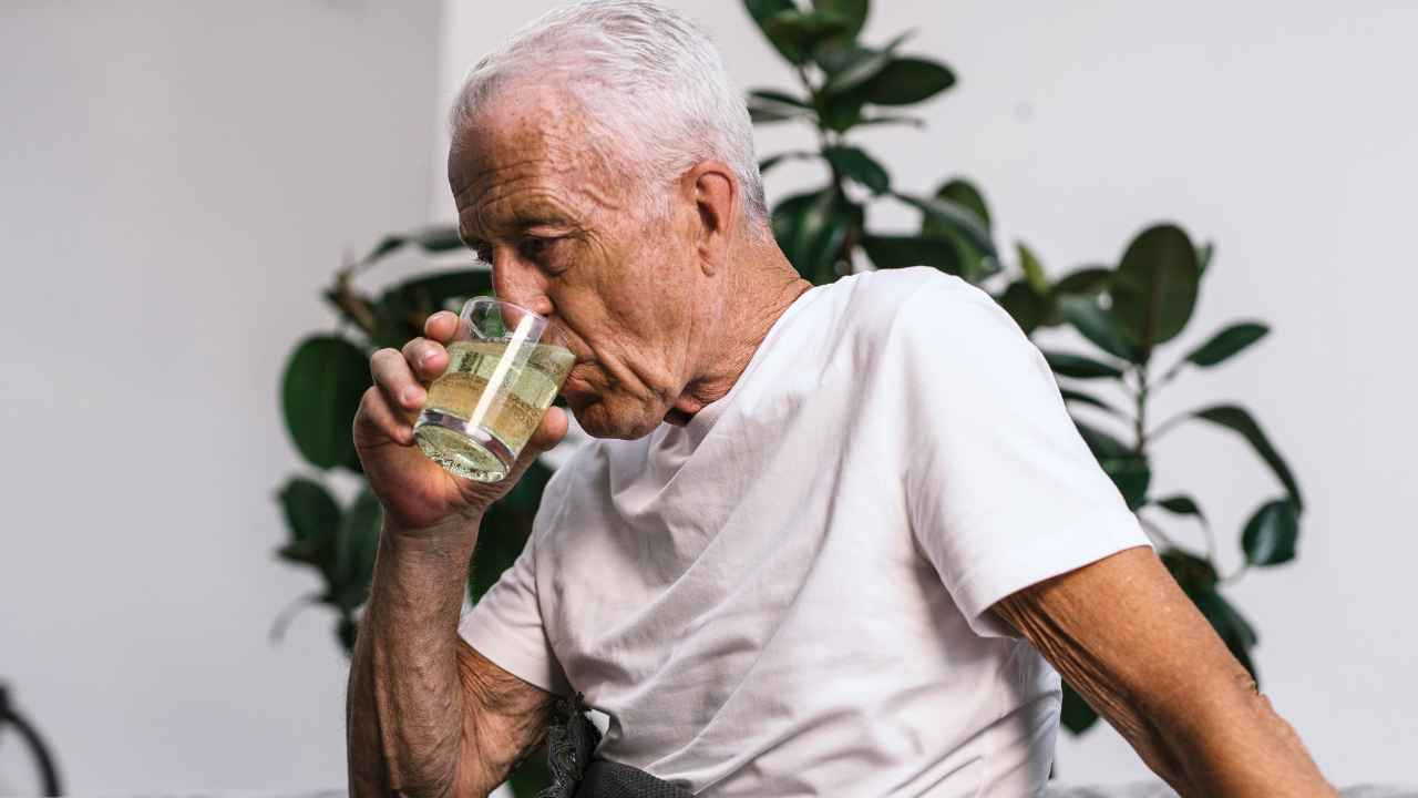 Hombre mayor bebiendo un vaso de agua en casa