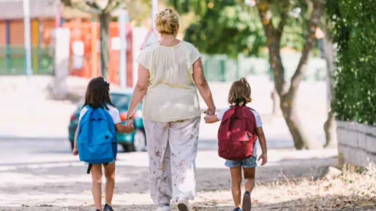 Persona adulta caminando con dos menores con mochilas en un entorno escolar