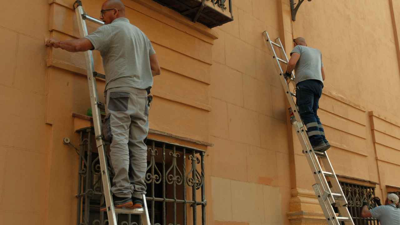 Trabajadores realizando tareas de mantenimiento en la fachada de un edificio desde escaleras.