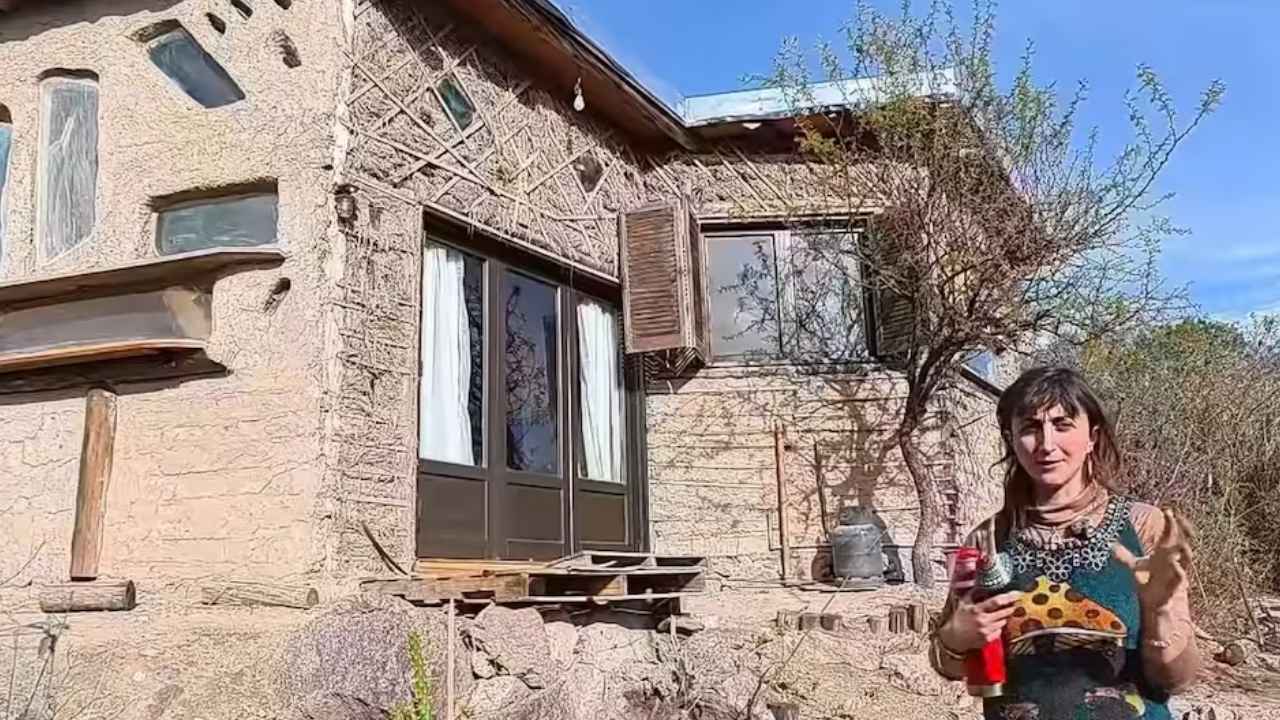 Mariana junto a la casa de barro construida con parabrisas y materiales reutilizados en Los Hornillos