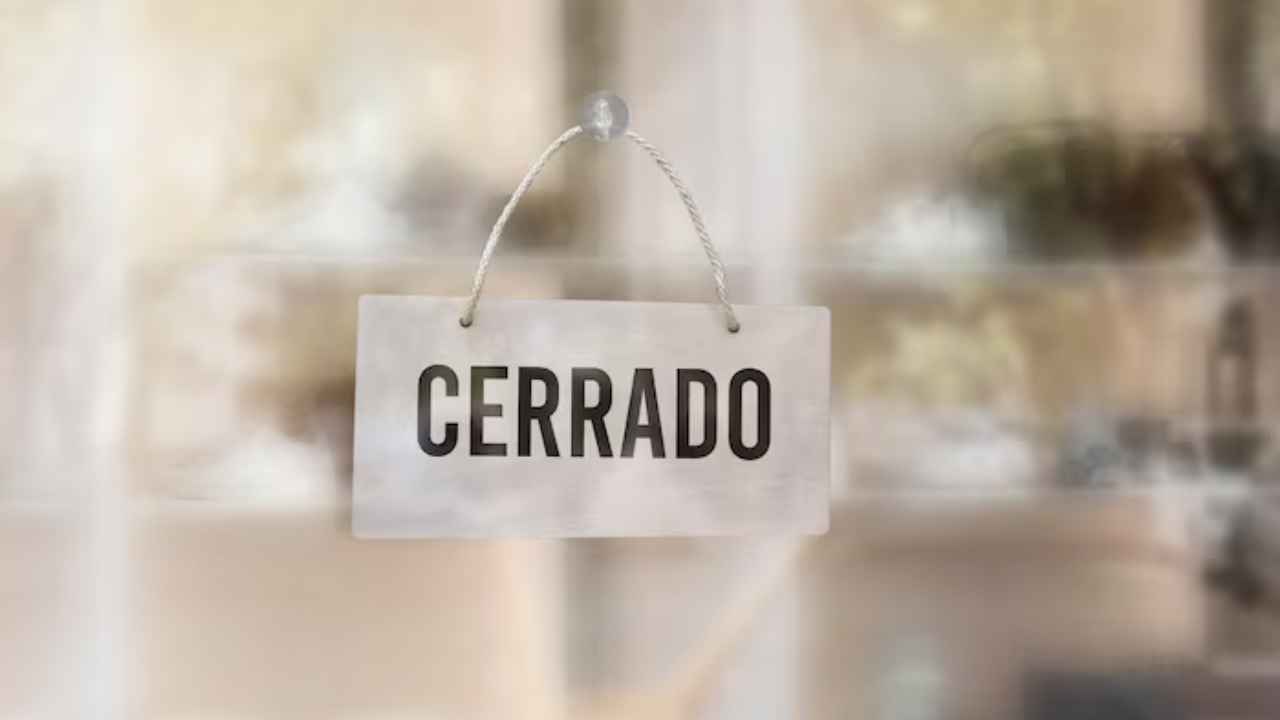 Empresario baja la persiana de un pequeño comercio junto a un trabajador