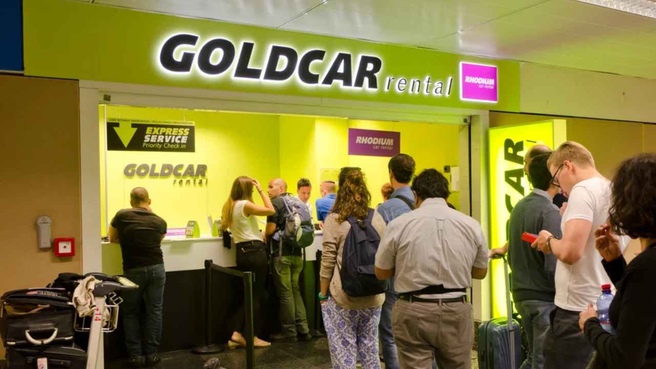 Oficina de Goldcar con clientes esperando en el mostrador de alquiler de coches