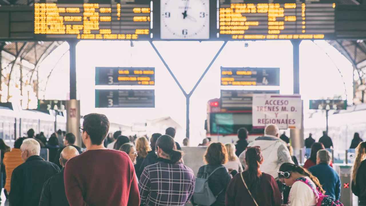 Viajeros frente a paneles de salidas y un reloj en una estación de Valencia.