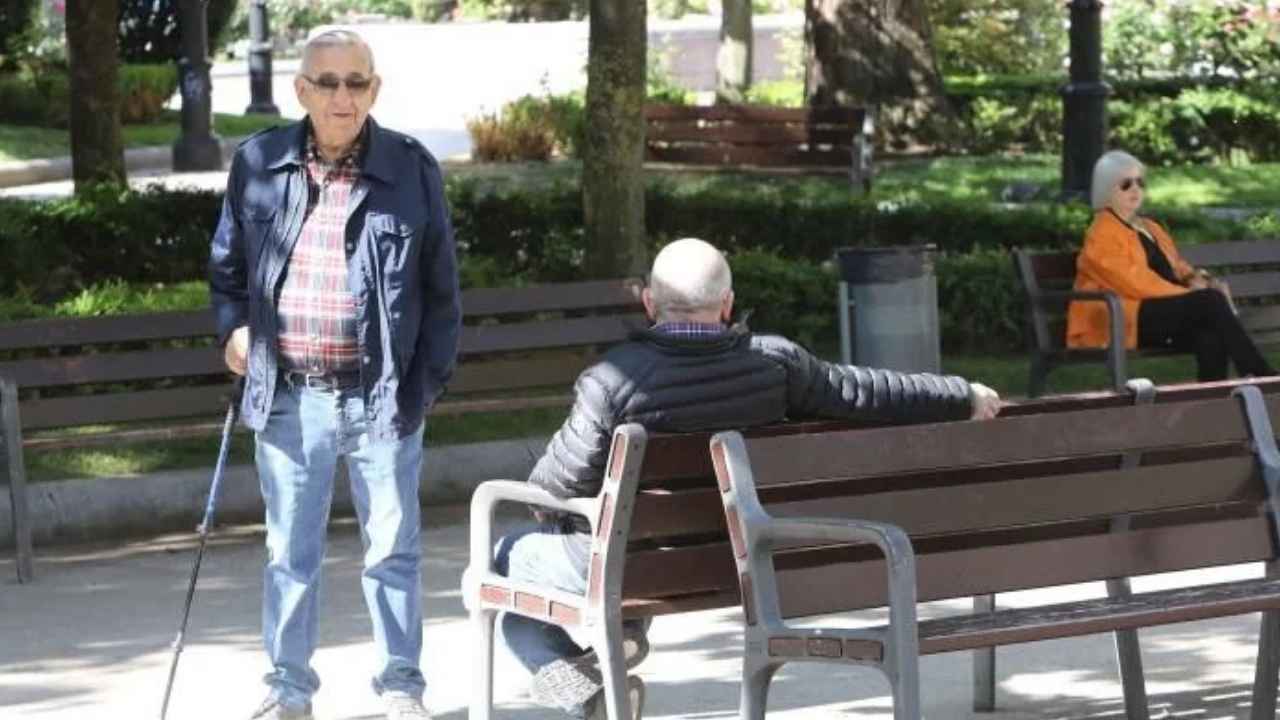 Jubilados en un parque, uno de ellos de pie junto a varios bancos