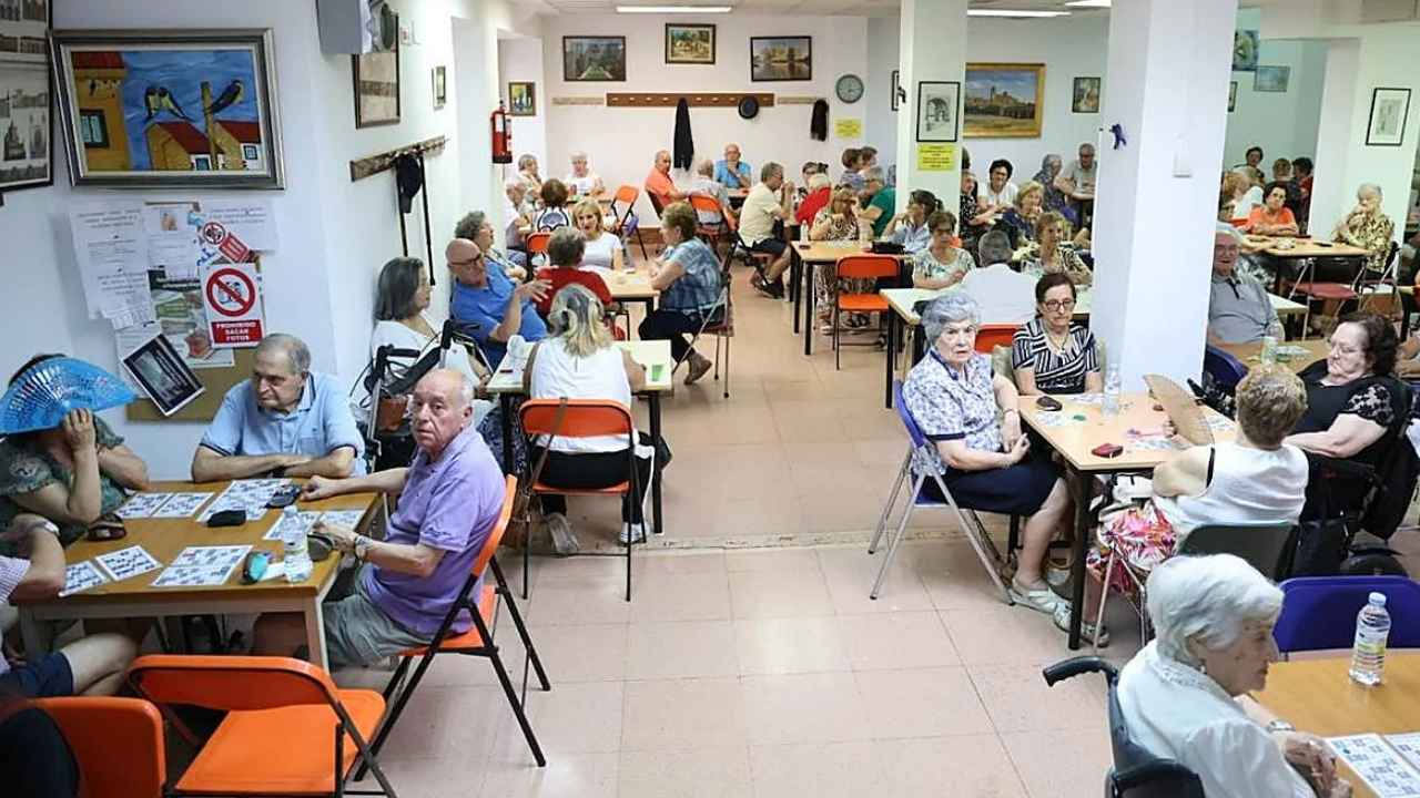 Personas mayores sentadas en torno a varias mesas durante una actividad en un centro social.