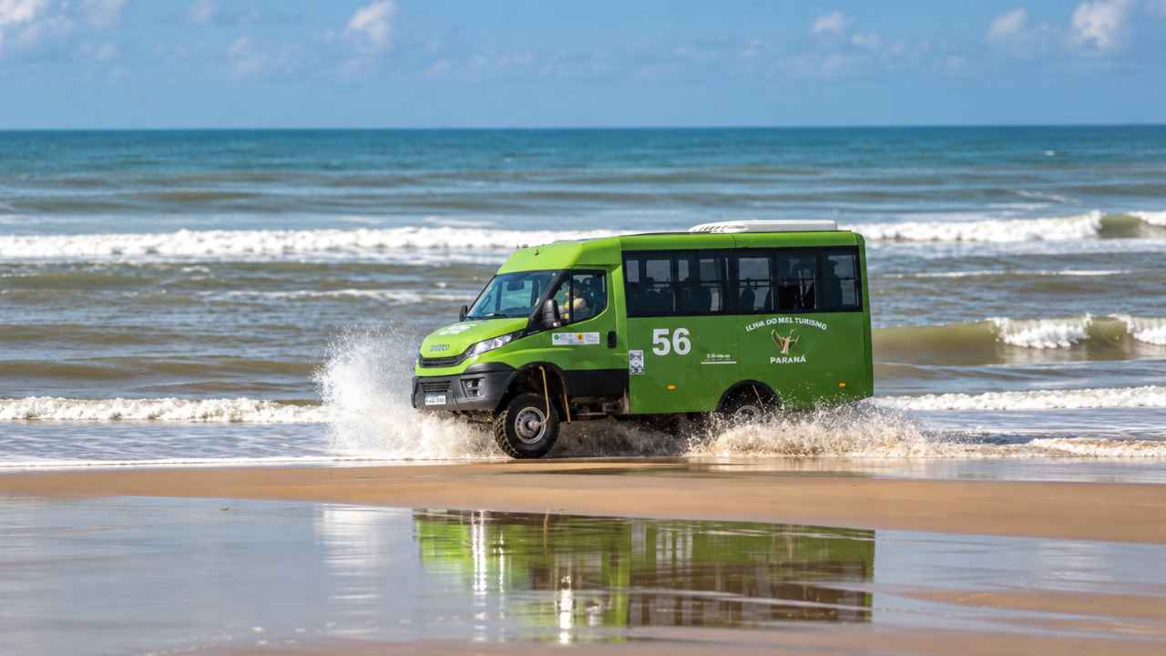 Minibús turístico 4x4 verde circulando por la orilla de una playa.