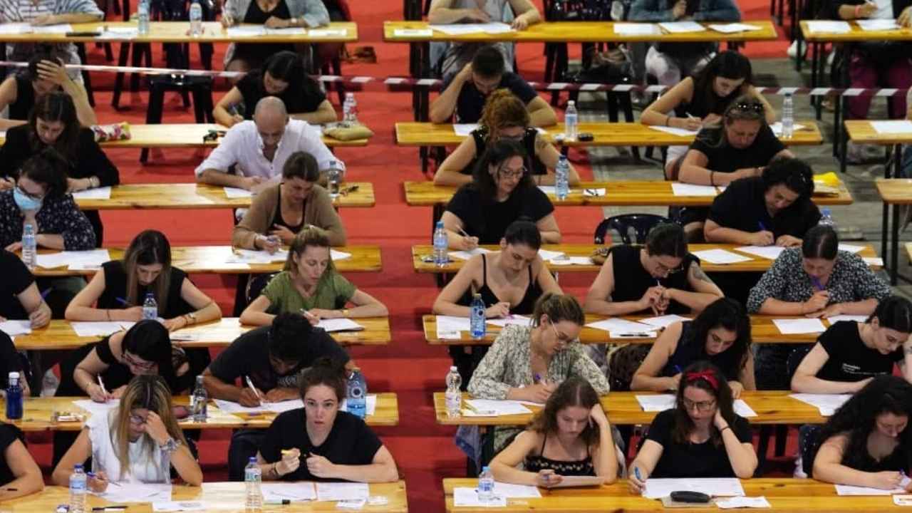 Aspirantes realizando un examen de oposición en un aula con varias filas de mesas