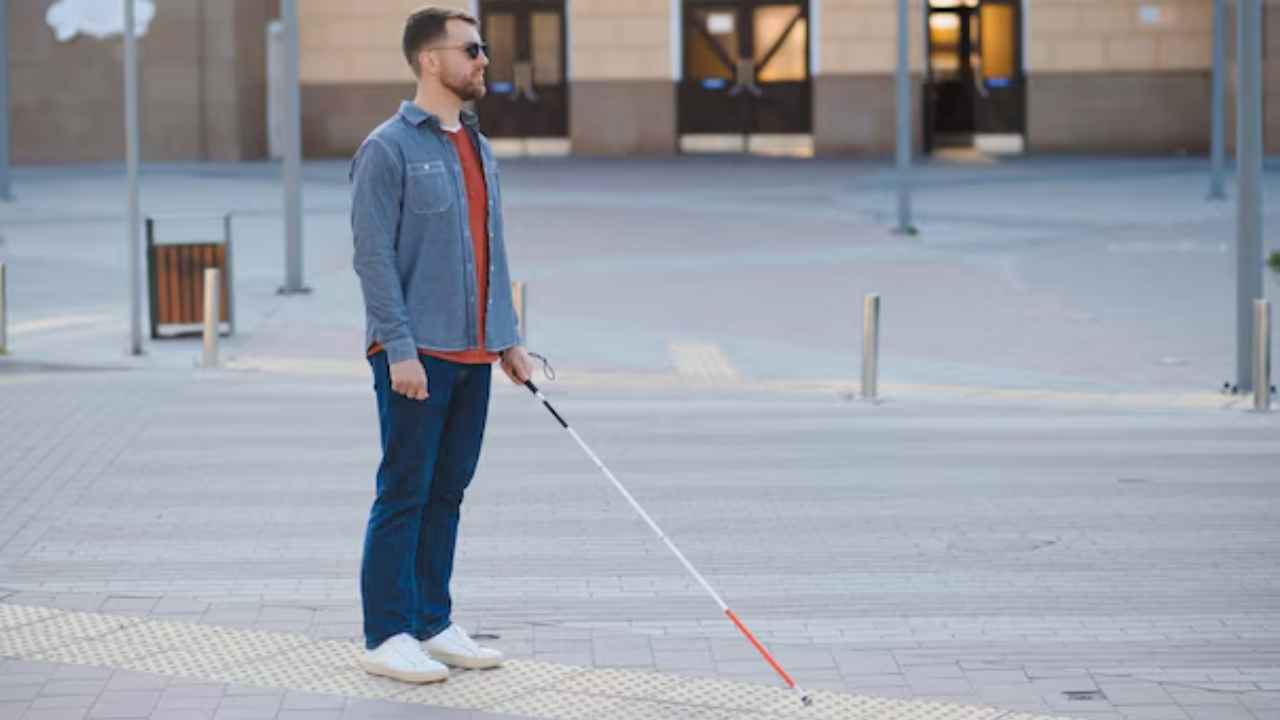 Hombre con ceguera caminando con bastón blanco por una zona urbana