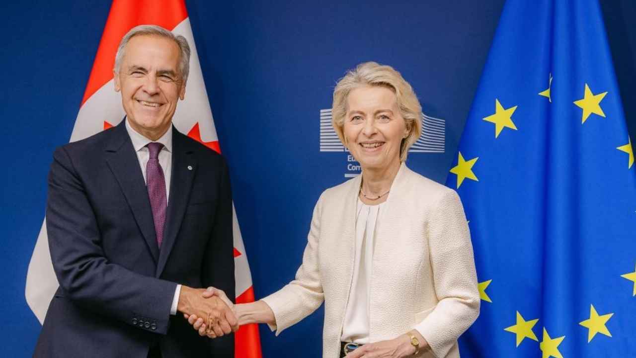 El primer ministro de Canadá y la presidenta de la Comisión Europea se estrechan la mano junto a las banderas de Canadá y la UE