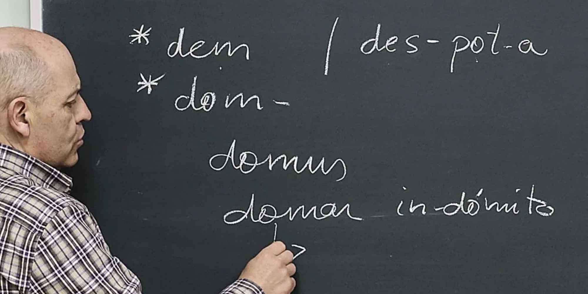 Profesor señalando con una tiza palabras en latín escritas en una pizarra.