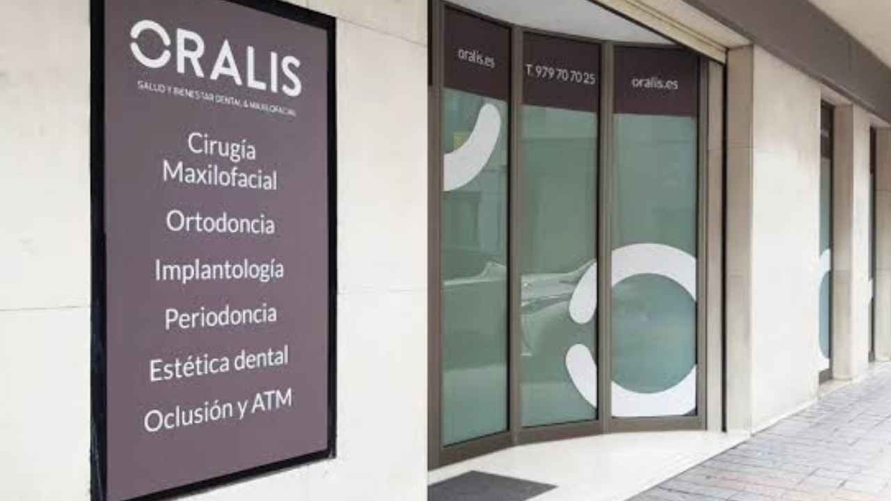 Fachada de una clínica dental Oralis con el logotipo de la empresa y un cartel de servicios de odontología y ortodoncia.