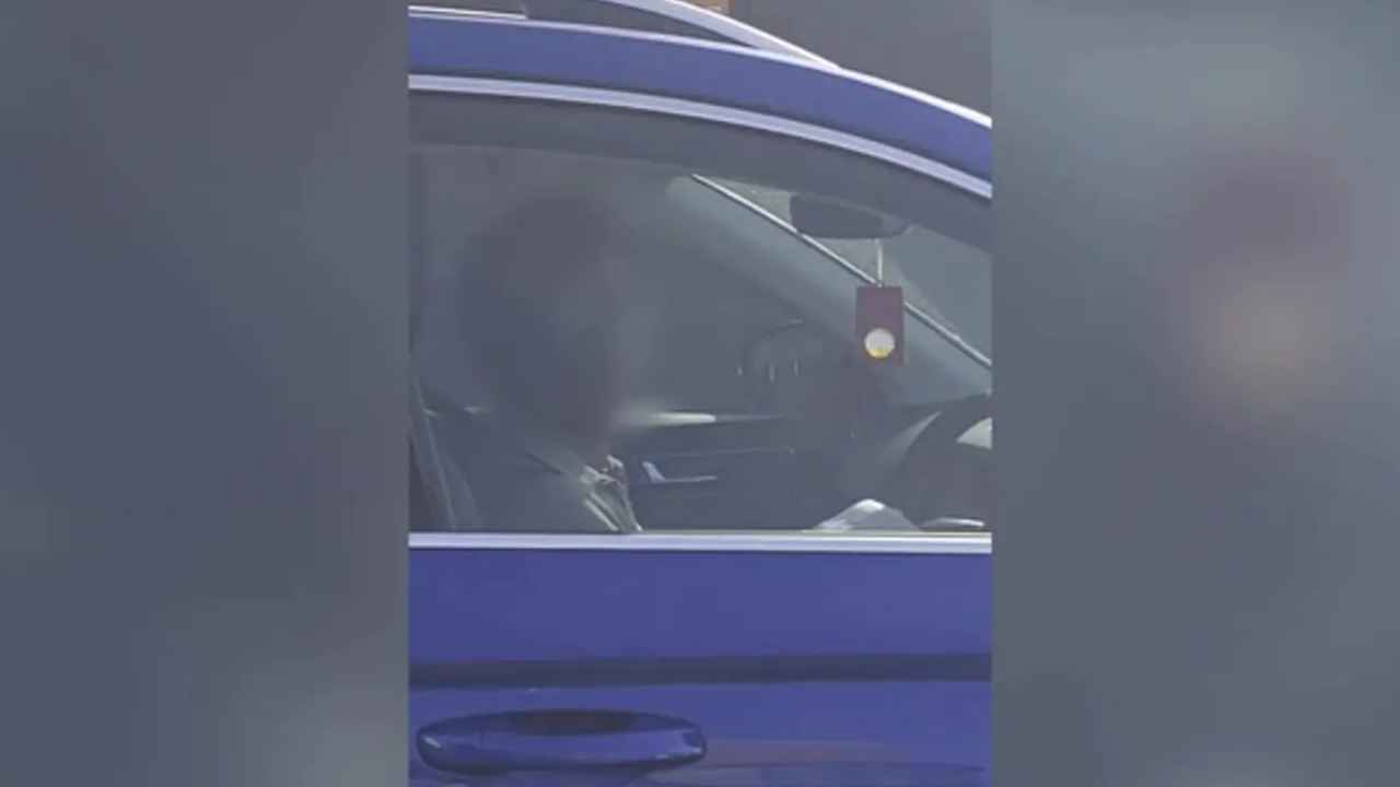 Conductora al volante de un coche azul, vista desde la ventanilla lateral en Guildford.