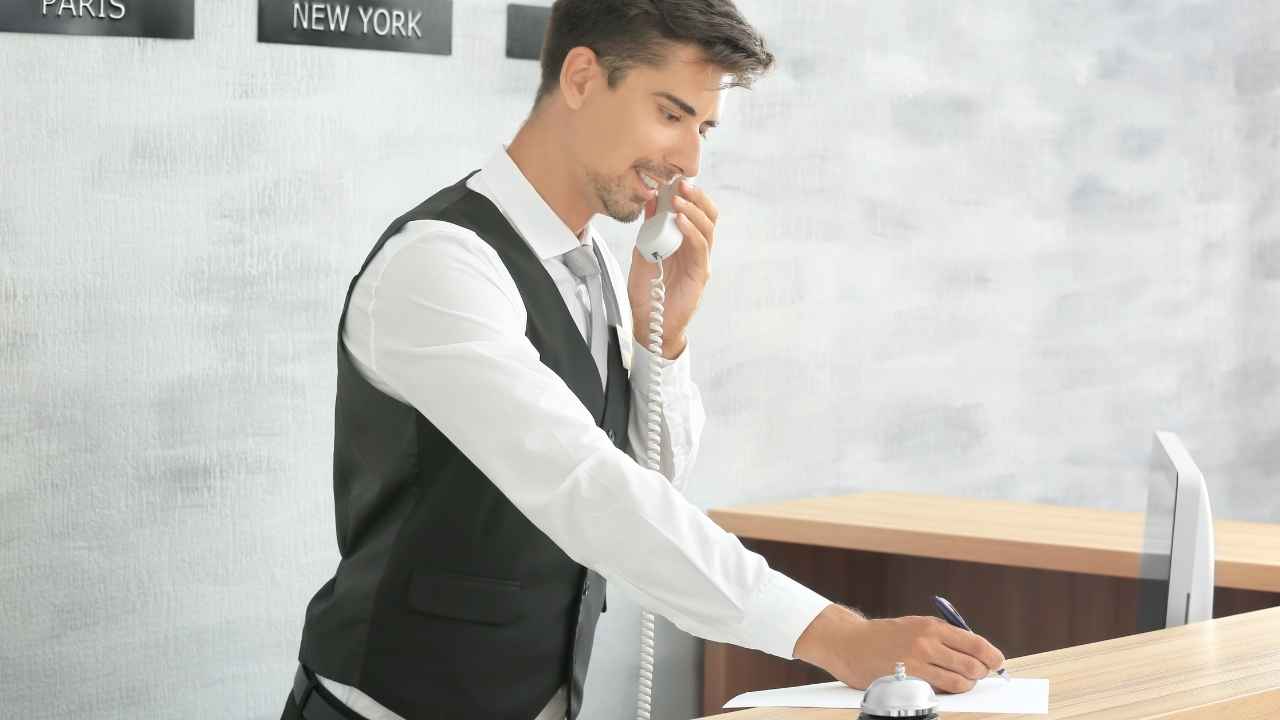 Hombre con camisa blanca y corbata azul trabajando ante un ordenador en un mostrador de recepción.