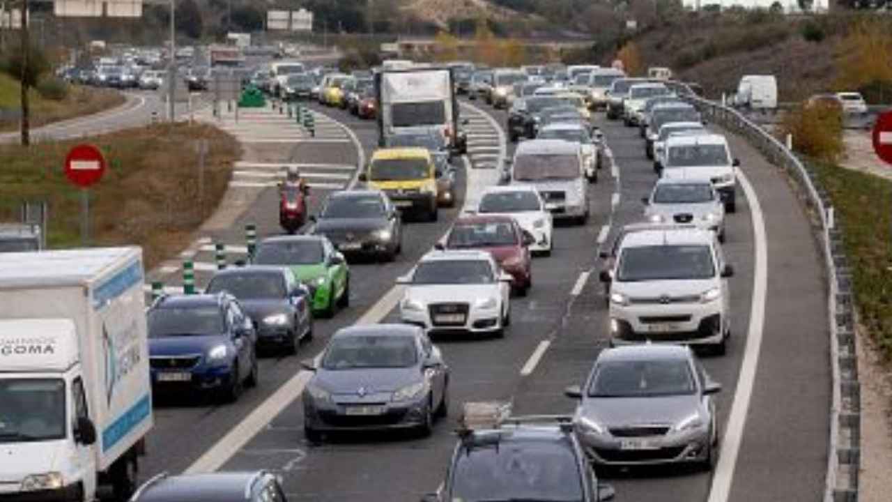 Retención de tráfico con numerosos coches, furgonetas y camiones circulando lentamente por una autovía congestionada.