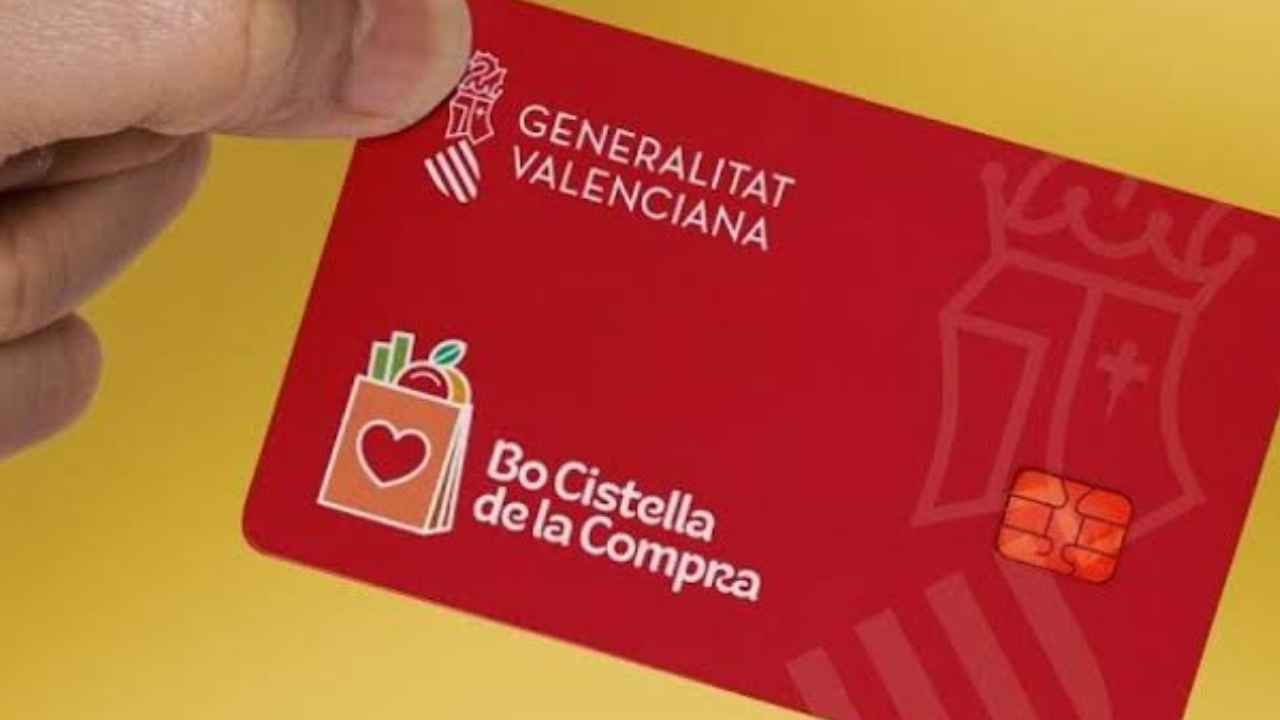 Una mano sostiene la tarjeta roja Bo Cistella de la Compra de la Generalitat Valenciana, destinada a ayudas para productos básicos.