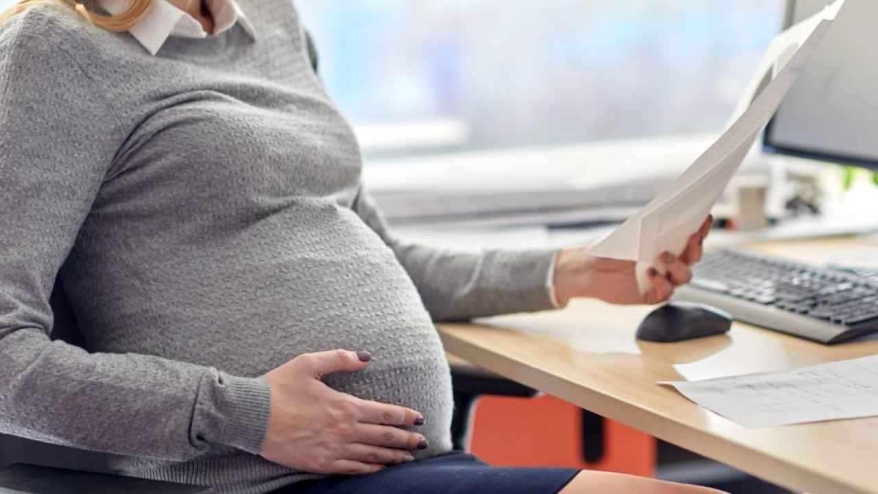 Mujer embarazada trabajando en una oficina mientras revisa documentos junto a un ordenador