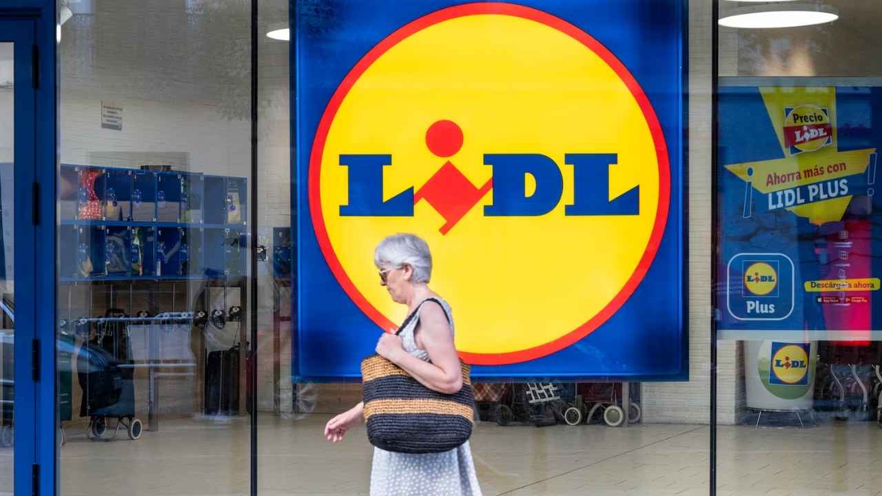 Una mujer camina frente a un supermercado Lidl con el logotipo de la cadena en el escaparate.