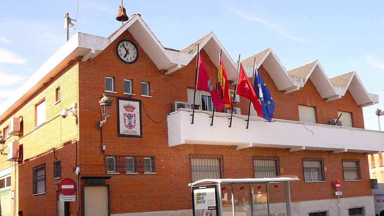 Fachada de ladrillo del Ayuntamiento de Loeches con reloj, escudo y banderas