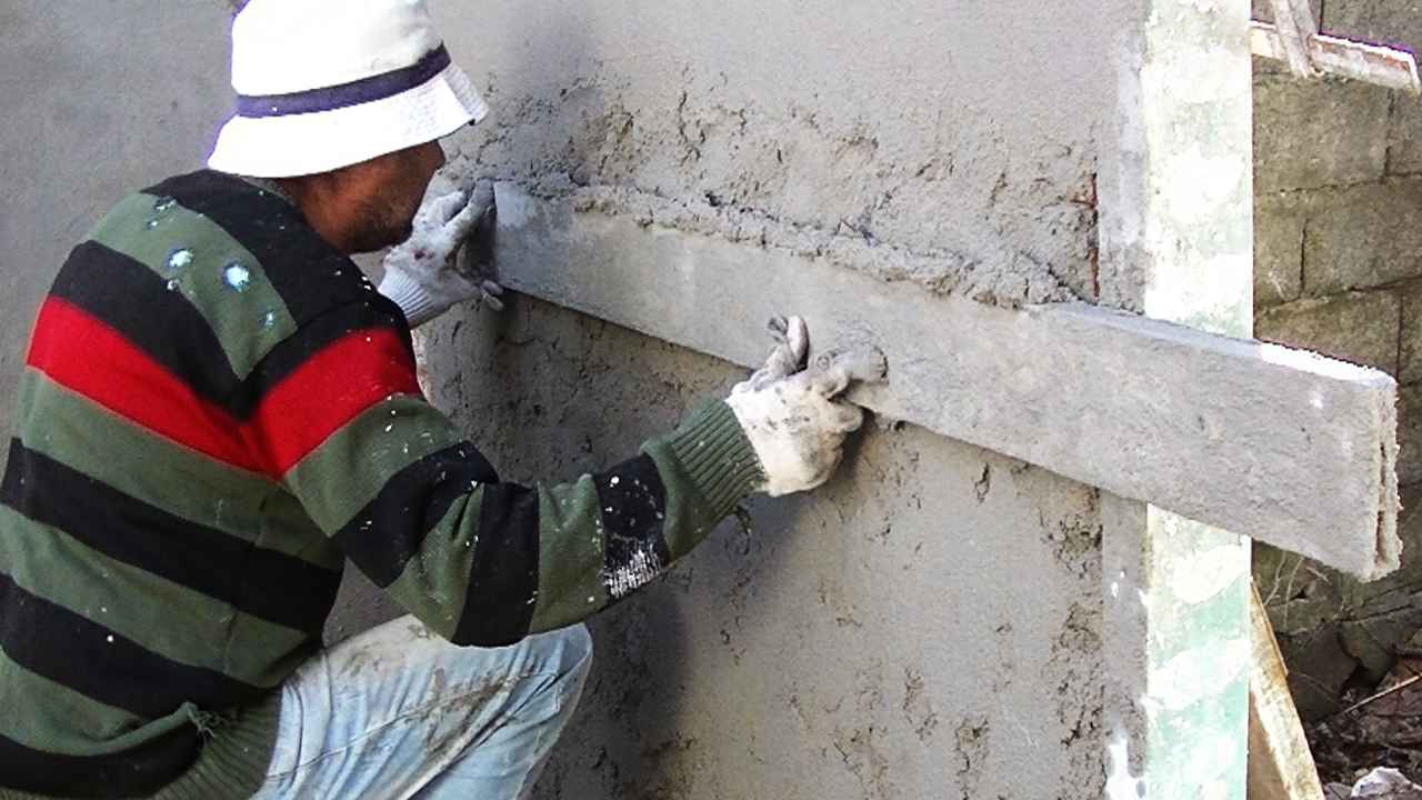 Albañil con guantes alisando el revestimiento de una pared con una regla.