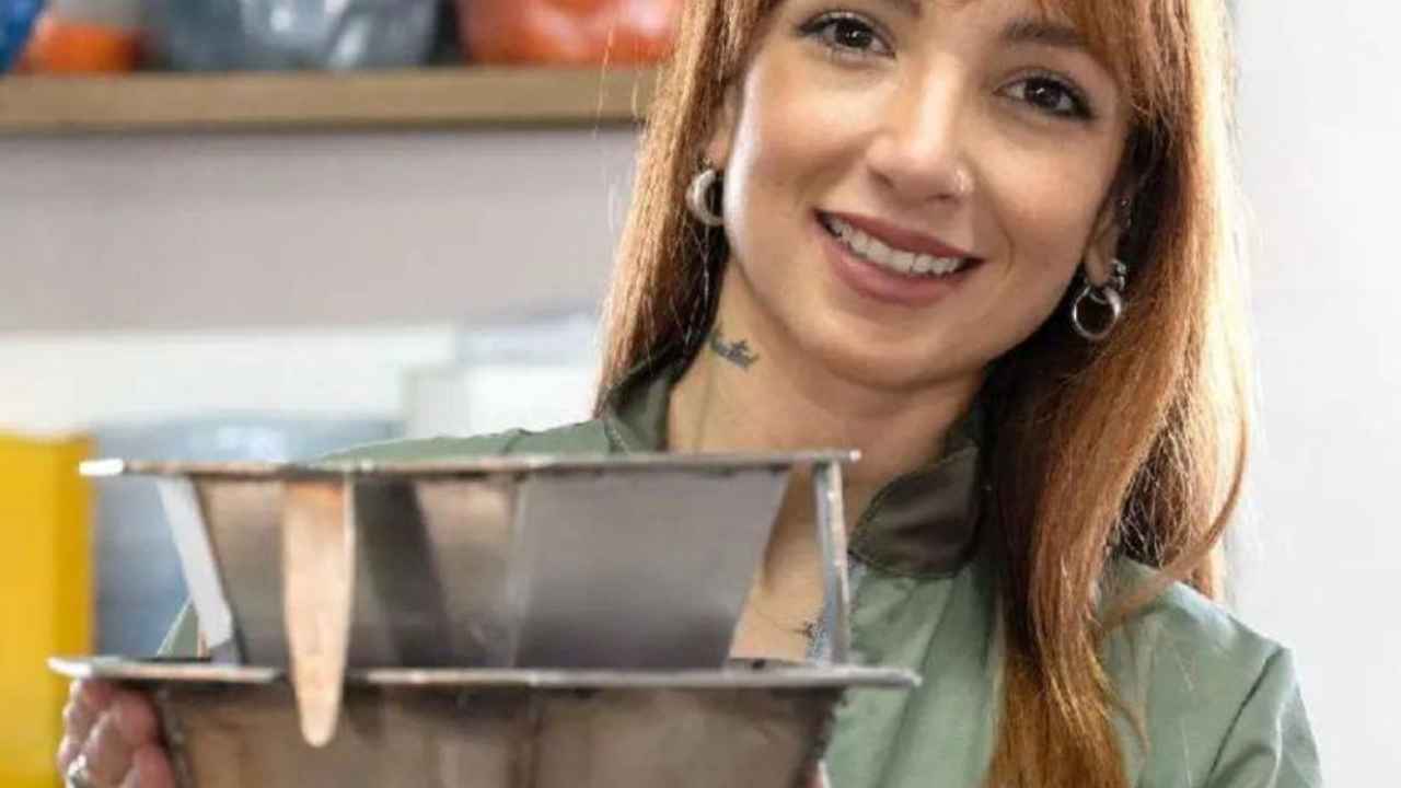 Mujer sosteniendo dos moldes metálicos en un taller de reciclaje de plástico.