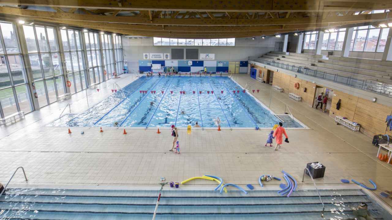 Interior de una piscina cubierta municipal con varias personas nadando y amplias instalaciones deportivas.