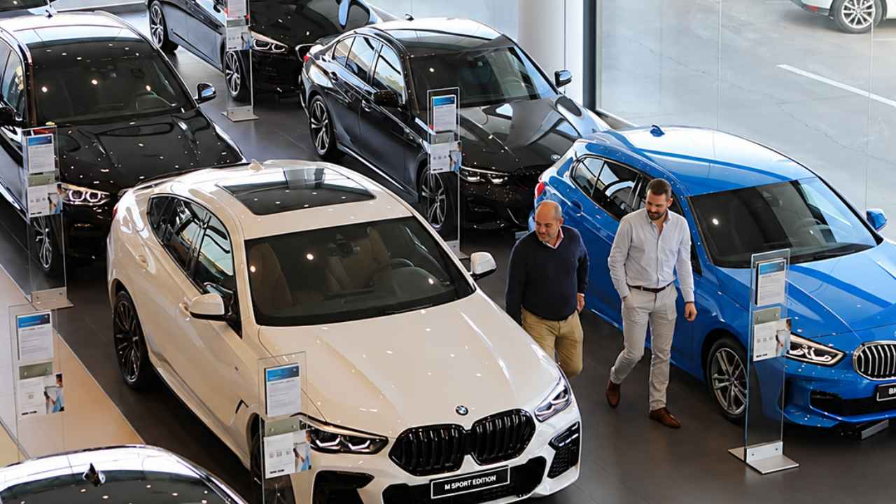 Varios coches BMW nuevos expuestos en un concesionario, con dos personas caminando entre los vehículos.