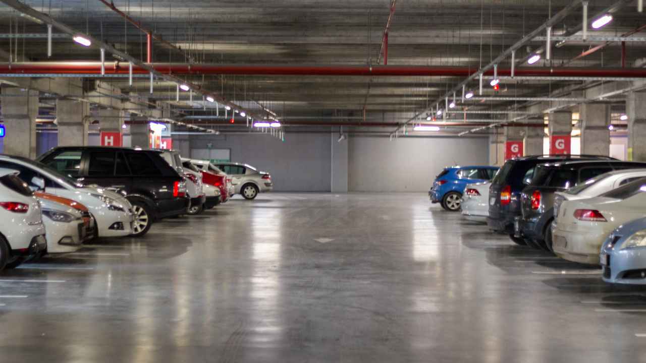 Aparcamiento comunitario subterráneo con varias plazas de garaje ocupadas por coches a ambos lados.