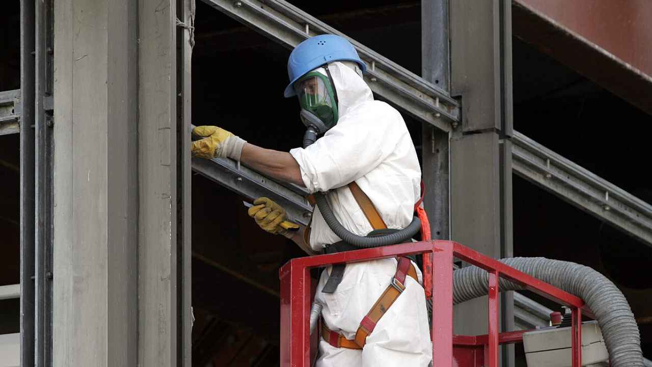 Trabajador con casco, mascarilla y traje blanco en una plataforma junto a una estructura metálica