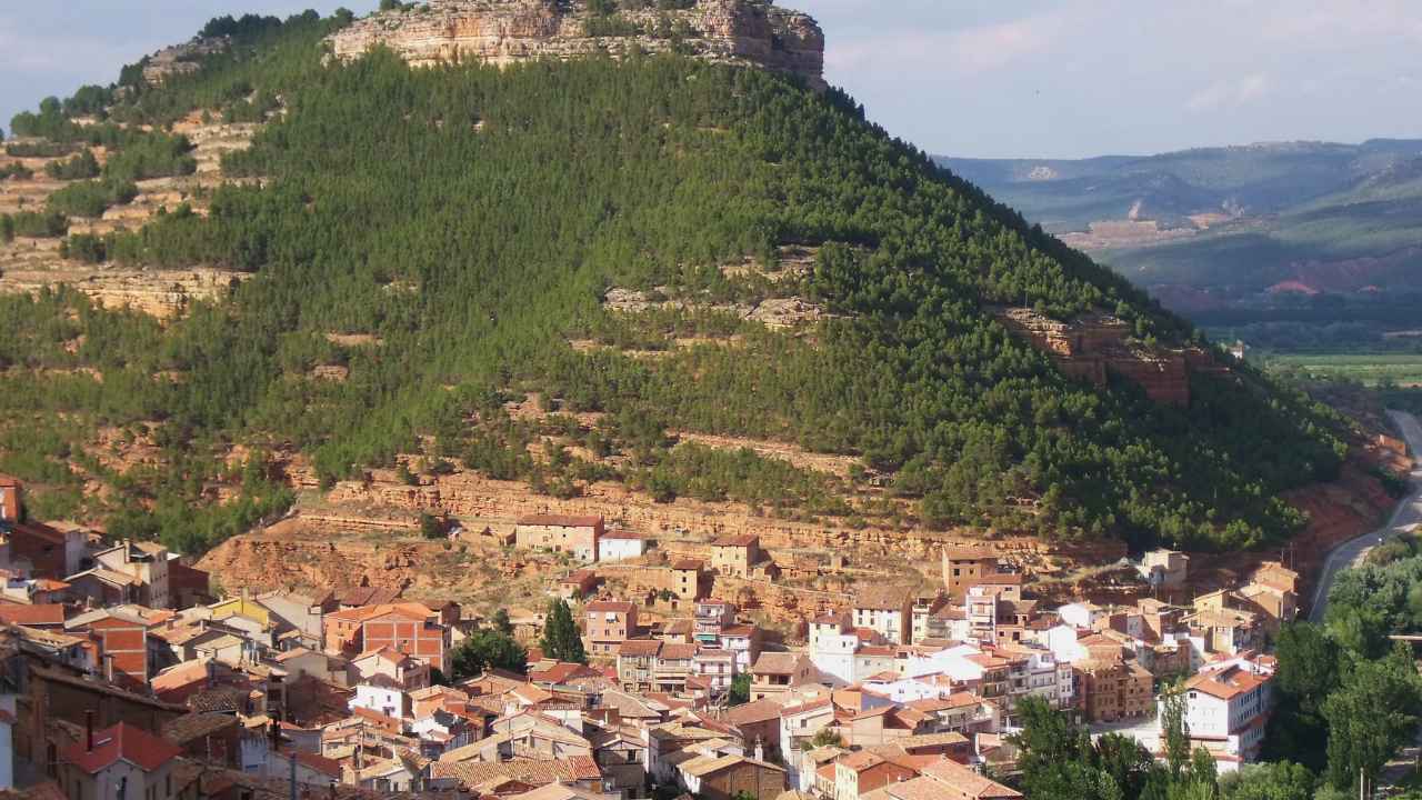Vista panorámica de Santa Cruz de Moya, en Cuenca, con casas de tejados rojizos al pie de una montaña arbolada.