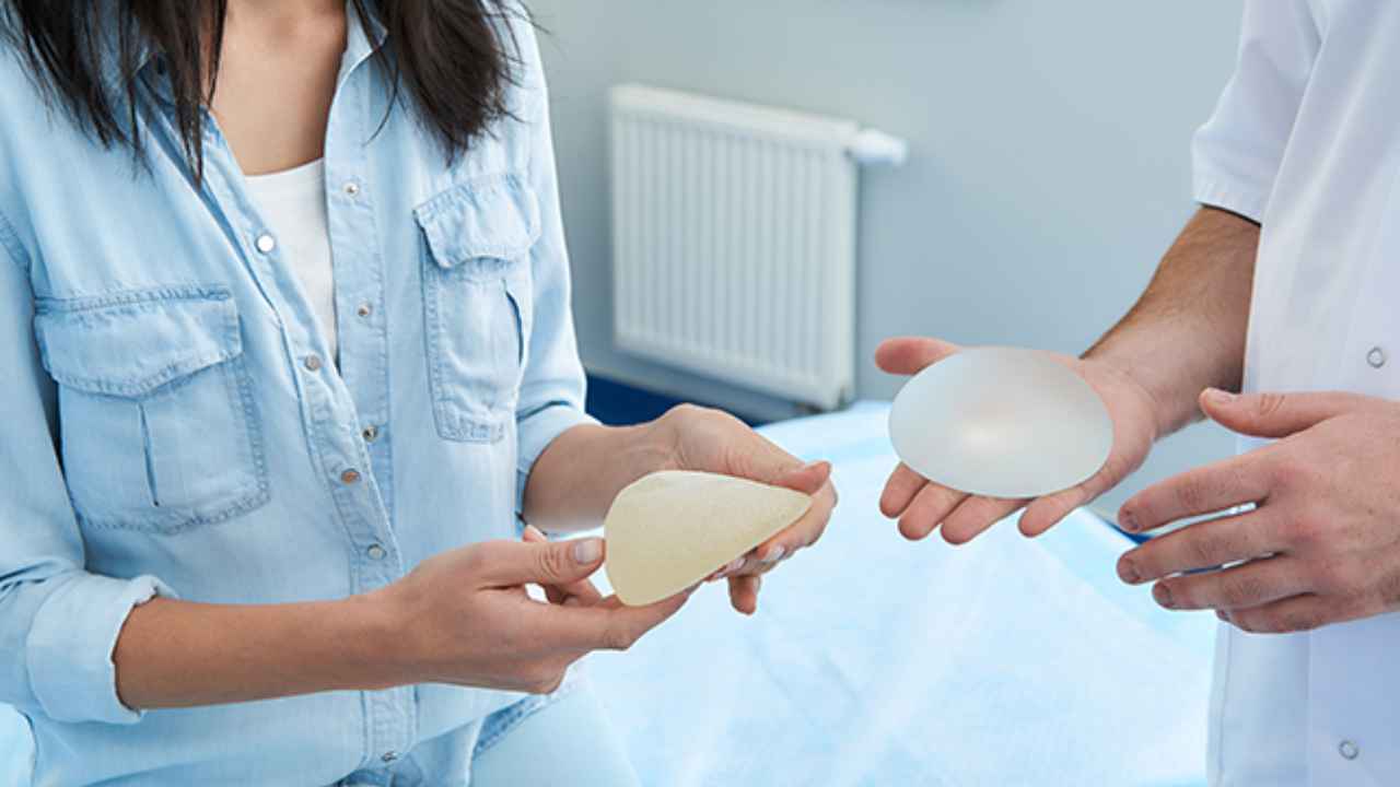 Mujer y profesional sanitario mostrando dos prótesis mamarias durante una consulta médica sobre implantes de pecho.