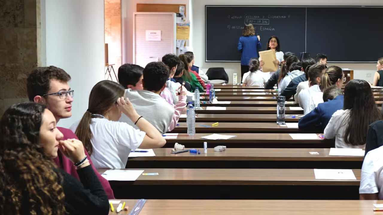 Estudiantes universitarios asisten a una clase presencial en un aula, mientras dos profesoras imparten la sesión.