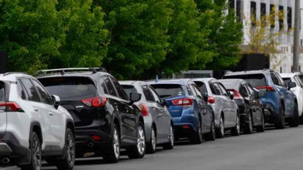Fila de coches aparcados junto a viviendas y árboles en una calle residencial.