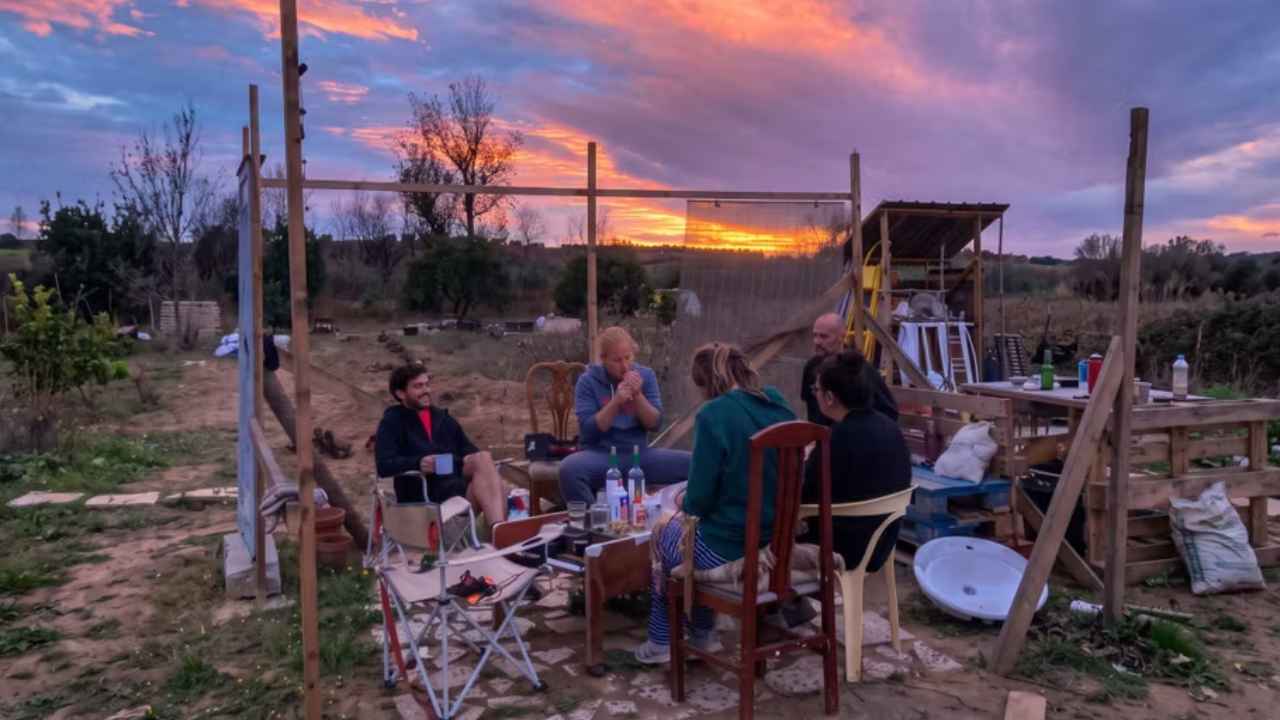 Grupo de cinco personas reunidas al atardecer en una finca, junto a una estructura de madera.
